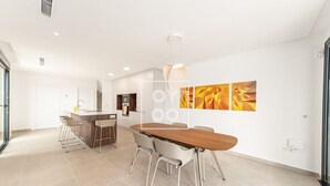 Eine moderne Küche mit Kochinsel, ein Essbereich mit Holztisch und Stühlen sowie ein Wohnbereich mit Sofa und Fernseher.
