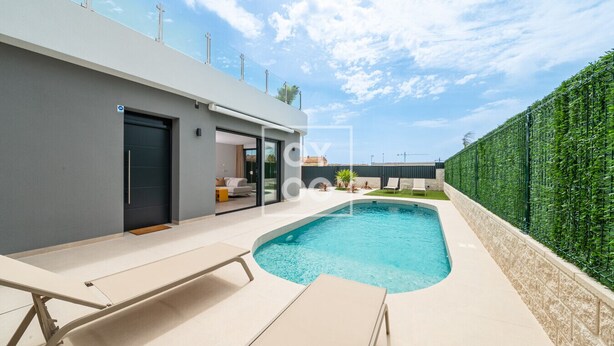 Ein modernes Haus mit Swimmingpool, überdachter Terrasse und einer grünen Hecke.
