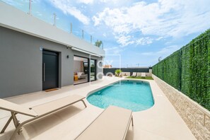 Ein modernes Haus mit Swimmingpool, überdachter Terrasse und einer grünen Hecke.
