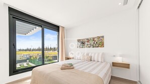 Ein Schlafzimmer mit großem Fenster, einem Bett mit gestreifter Bettwäsche, einem Nachttisch mit Lampe und einer Wand mit farbenfroher abstrakter Kunst.