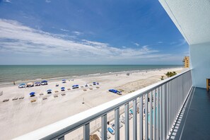 A balcony with a view of a beach, a building with a yellow facade, and a clear sky. - Direct Beachfront Penthouse (Indian Shores)