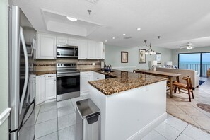 A modern kitchen with white cabinets, stainless steel appliances, and a granite countertop island. - Direct Beachfront Penthouse (Indian Shores)