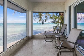 A balcony with a view of the ocean, equipped with chairs and a table. - Cayman Luxury Rentals at Tamarind Bay (Seven Mile Beach)