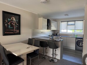 A compact kitchen with a dining area, a washing machine, and a large window.