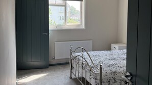 Un dormitorio con cama, radiador, ventana y puerta.