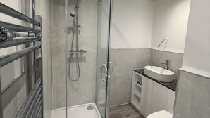 Un baño moderno con cabina de ducha de vidrio, un lavabo blanco y un inodoro.