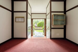 Ein Flur mit rotem Teppich, der zu einer Tür führt, einem Bilderrahmen an der linken Wand und einem Holzschrank zur Rechten.