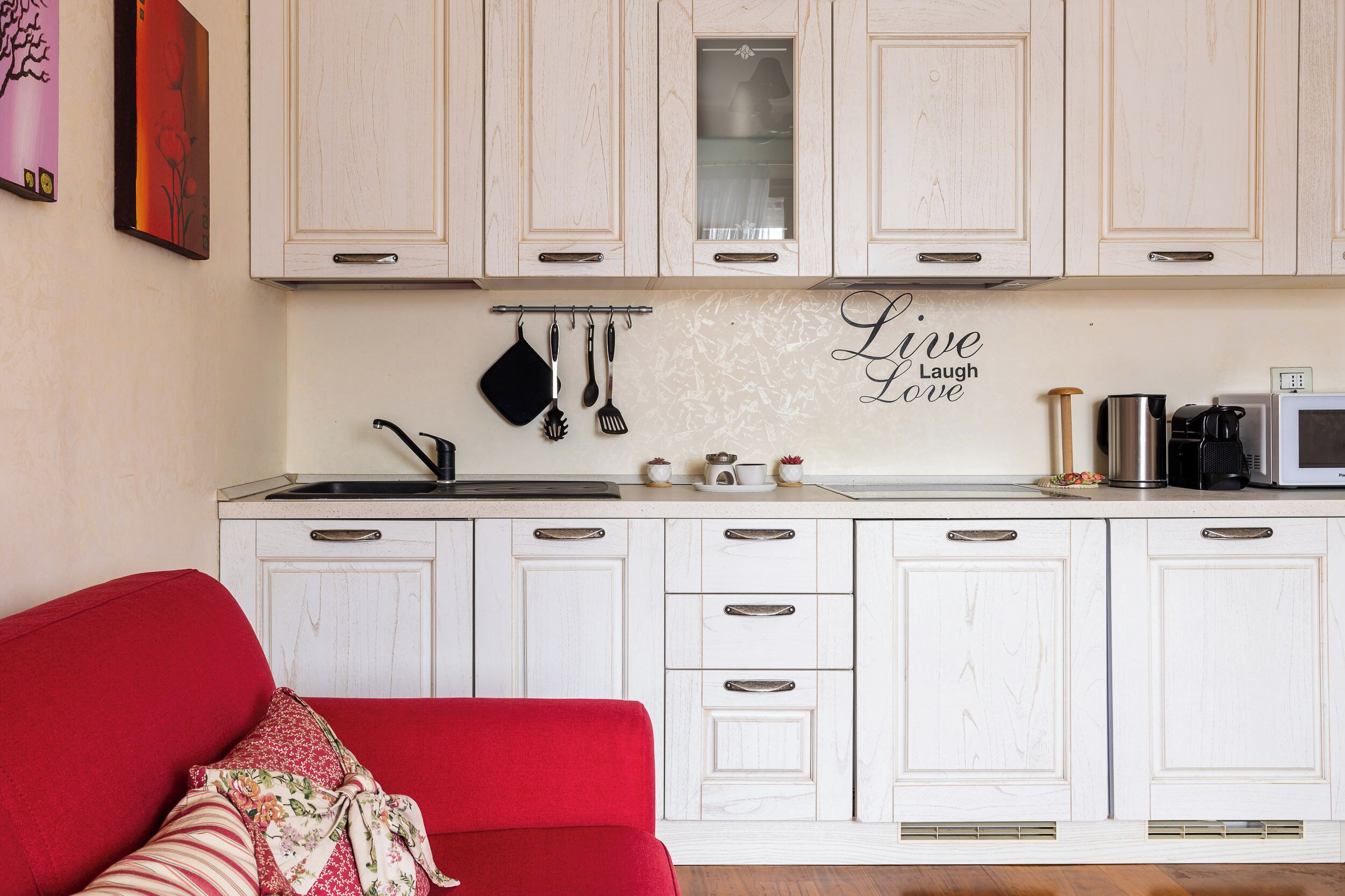 A kitchen with white cabinets, a red sofa, and a 'Live Laugh Love' sign.