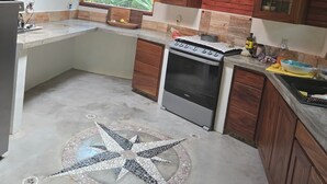 Een keuken met een vloerbedekking van starmotieven, houten keukenkastjes, een fornuis en een raam met uitzicht op groen.