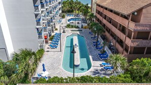 Ein Hotel mit einem zentralen Schwimmbad, mehreren Balkonen und Meerblick.