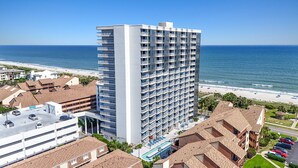 Ein Hochhotel mit mehreren Balkonen, einem Schwimmbad und Blick auf den Strand.