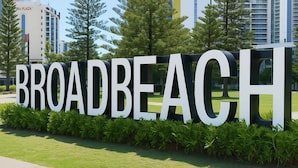 Un cartel con la palabra 'BROADBEACH' en letras grandes, rodeado de vegetación.