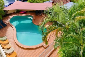 Ein Pool mit gewölbter Kante, umgeben von einer gefliesten Terrasse und Palmen.