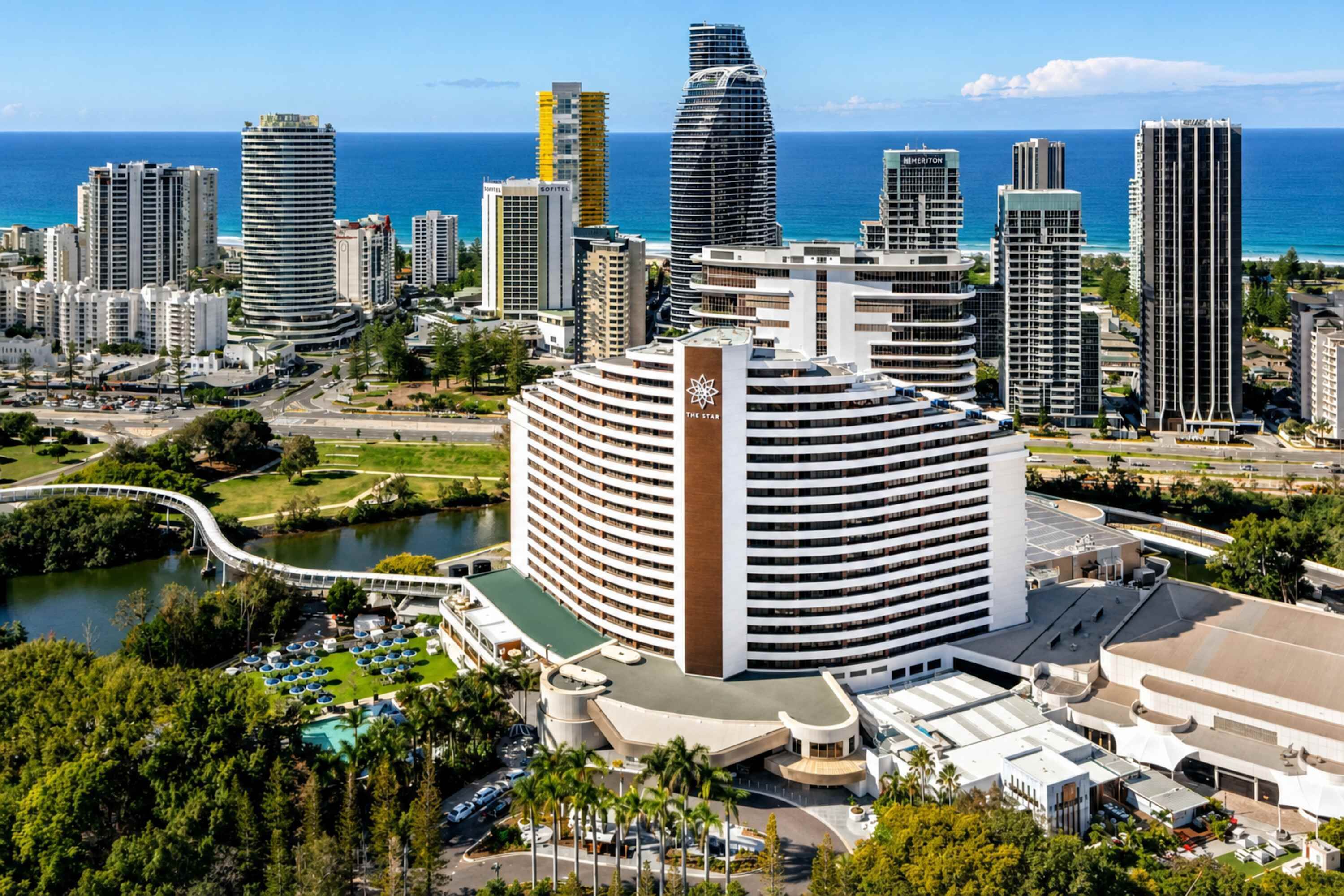 Un hôtel moderne à la façade incurvée, doté d’un logo bien visible et offrant une vue sur l’océan.