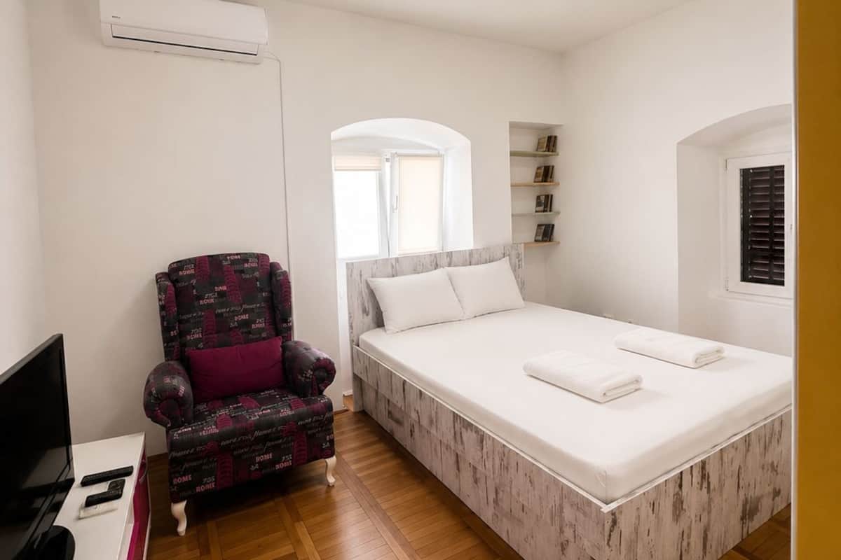 Un dormitorio con cama, una silla, televisor y aire acondicionado.