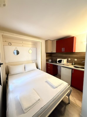 A hotel room with a bed, a small kitchenette, and a mirror on the wall.