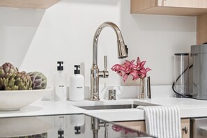 A modern kitchen with a stainless steel faucet, a bowl of artichokes, and two bottles of soap. - Casa Iglesia Apartment 201 (Santa Barbara)