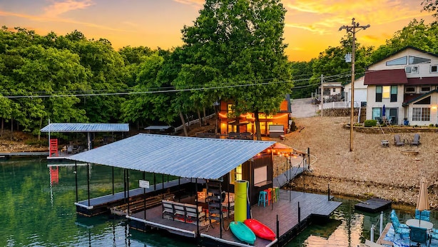 A waterfront property with a dock, outdoor seating, and a building with a covered patio.