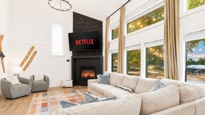 A modern living room with a fireplace, a flat-screen TV, and a large window with a view.