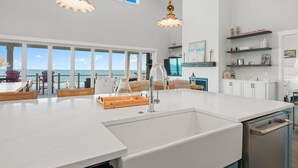 Une cuisine spacieuse dotée d’un grand îlot central, de meubles blancs et offrant une vue sur l’océan.
