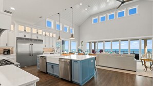 Une cuisine spacieuse dotée d’un grand îlot central, d’appareils électroménagers en acier inoxydable et offrant une vue sur l’océan.