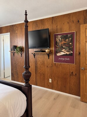 A bedroom with a four-poster bed, a television mounted on a wooden wall, and a framed picture of a garden. - Beautifully Remodeled 4BR Phoenix Desert Garden Retreat (Phoenix)