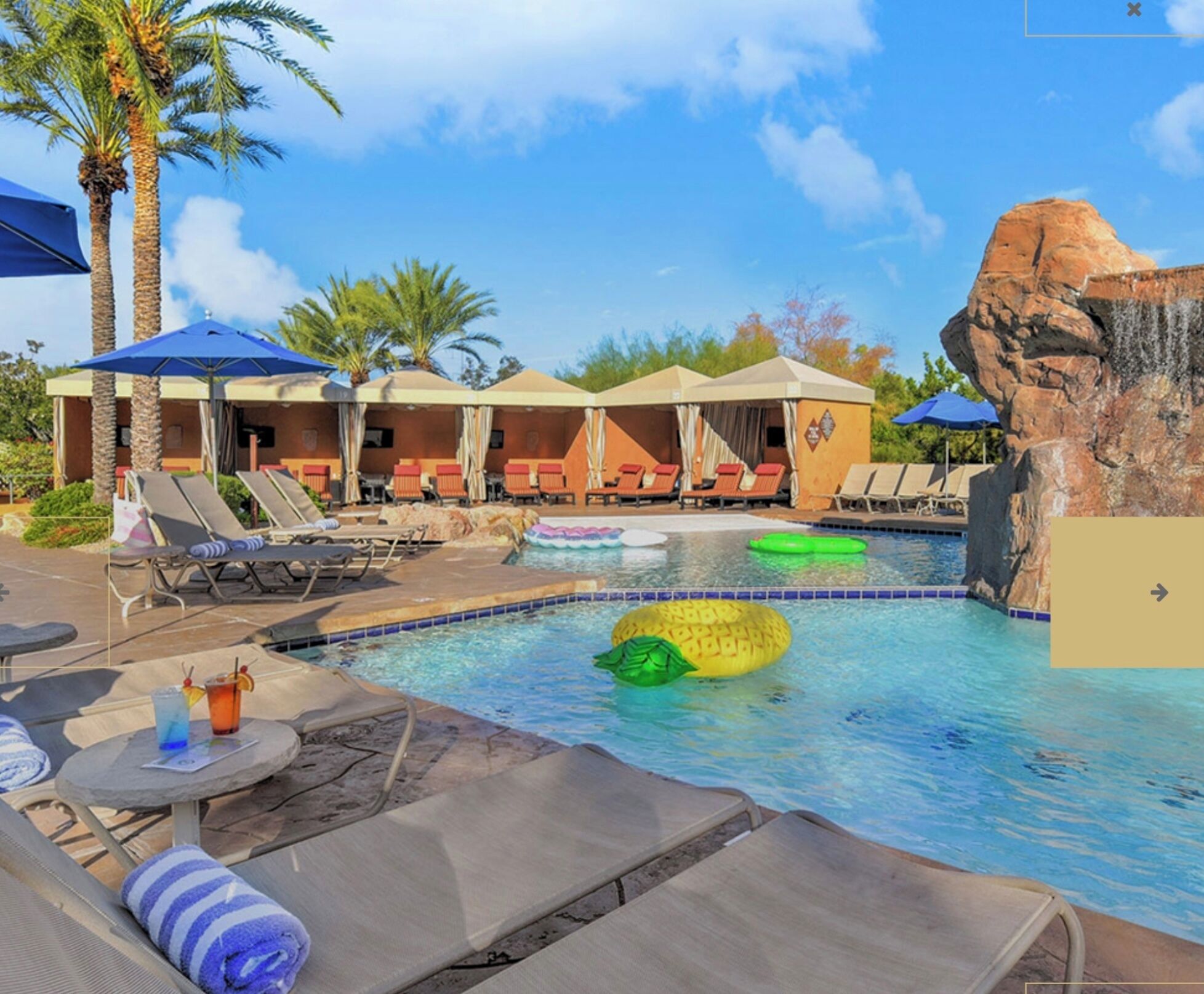 A pool area with lounge chairs, umbrellas, and a rock formation.