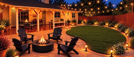 Une terrasse à l’arrière de la maison, avec un foyer, des sièges d’extérieur et des guirlandes lumineuses.
