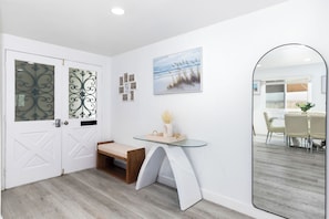 Ein modernes Interieur mit einer weißen Tür, einem Glastisch mit einer Vase, einer Bank und einem Gemälde an der Wand.
