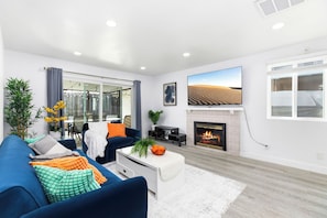 Ein modernes Wohnzimmer mit einem blauen Sofa, einem Kamin, einem Fernseher und einem großen Fenster.