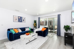Ein modernes Wohnzimmer mit einem blauen Sofa, einem weißen Couchtisch und einer Glastür, die auf einen Balkon führt.