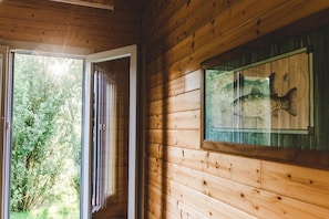 Interior de una cabaña de madera con un acuario de vidrio en la pared y una puerta que da a un jardín.