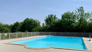 A rectangular swimming pool with a tiled deck, surrounded by a metal fence and trees in the background. - Accessible Family Cottage for 6 (Moncoutant-sur-Sèvre)
