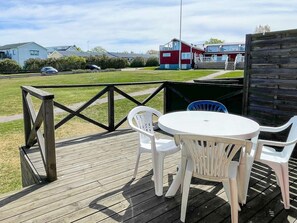 A wooden deck with a table and chairs, a fence, and houses in the background. - 4 Person Holiday Home in Kopingsvik (Kopingsvik)