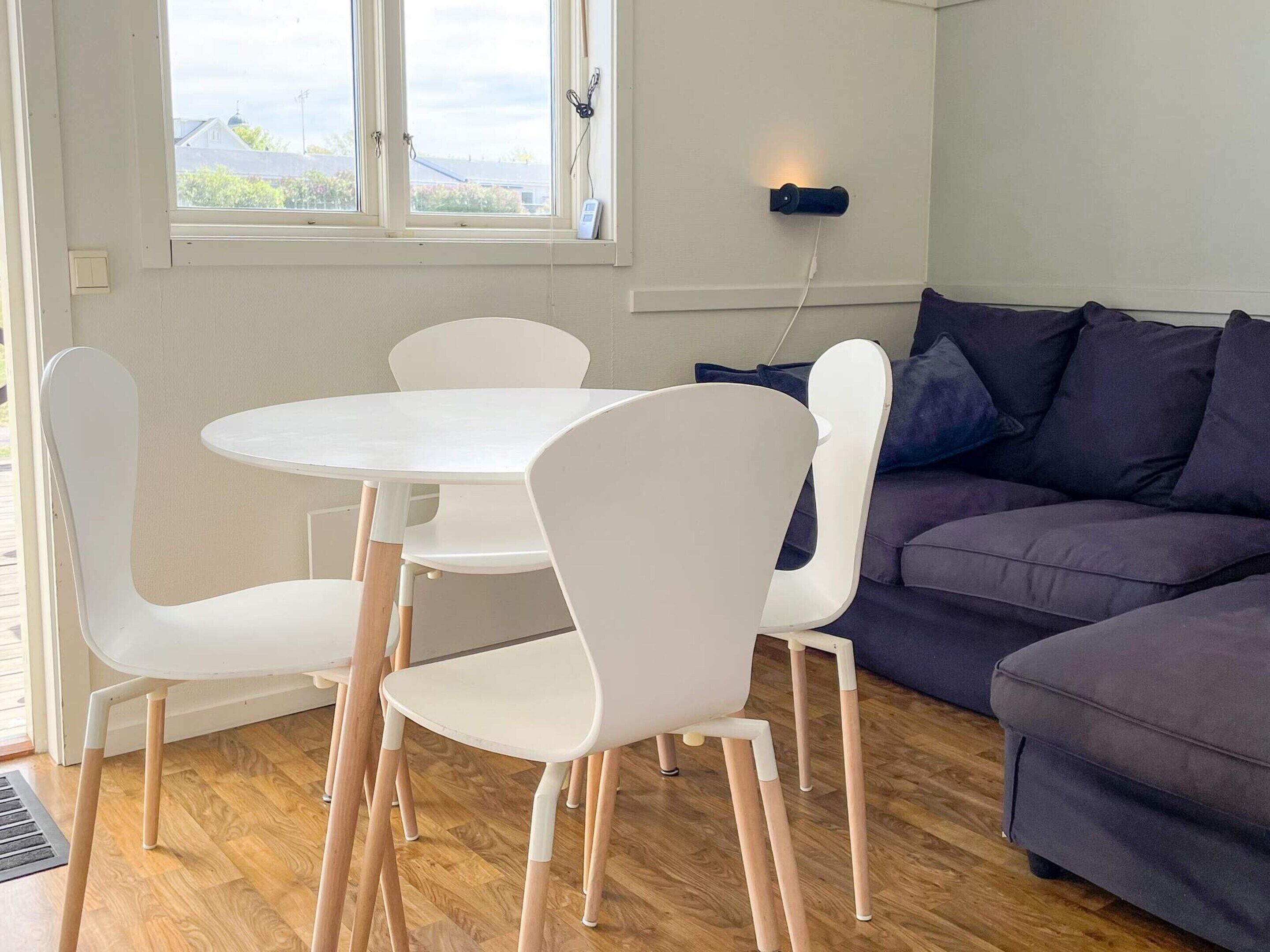 A room with a round table, four chairs, a sofa, and a window with a view of buildings.