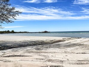 A beach with a pier extending into the water, a clear sky, and a tree on the left. - 4 Person Holiday Home in Kopingsvik (Kopingsvik)