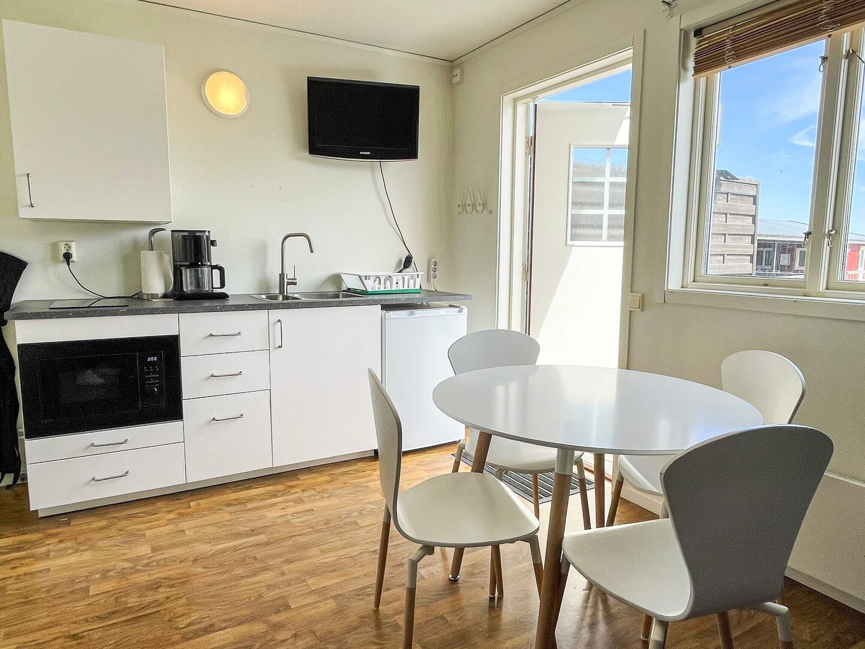 Cozinha compacta com micro-ondas, cafeteira e TV de tela plana. Possui área de jantar com mesa redonda e quatro cadeiras.