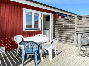 A red building with a white door and windows, a small outdoor table with chairs, and a wooden deck. - 4 Person Holiday Home in Kopingsvik (Kopingsvik)
