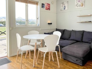 Ein Zimmer mit einem runden Tisch, vier Stühlen, einem grauen Sofa und einem Fenster mit Jalousien.
