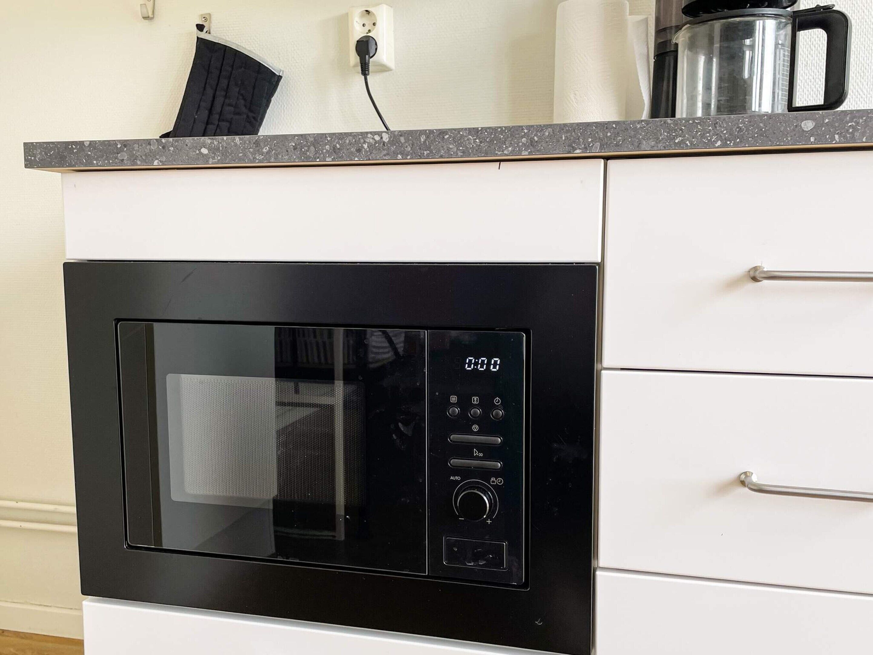 Una cocina con microondas integrado, cafetera y un enchufe en la encimera.