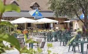 An outdoor seating area with tables and chairs, a restaurant sign, and a building with a sloped roof.