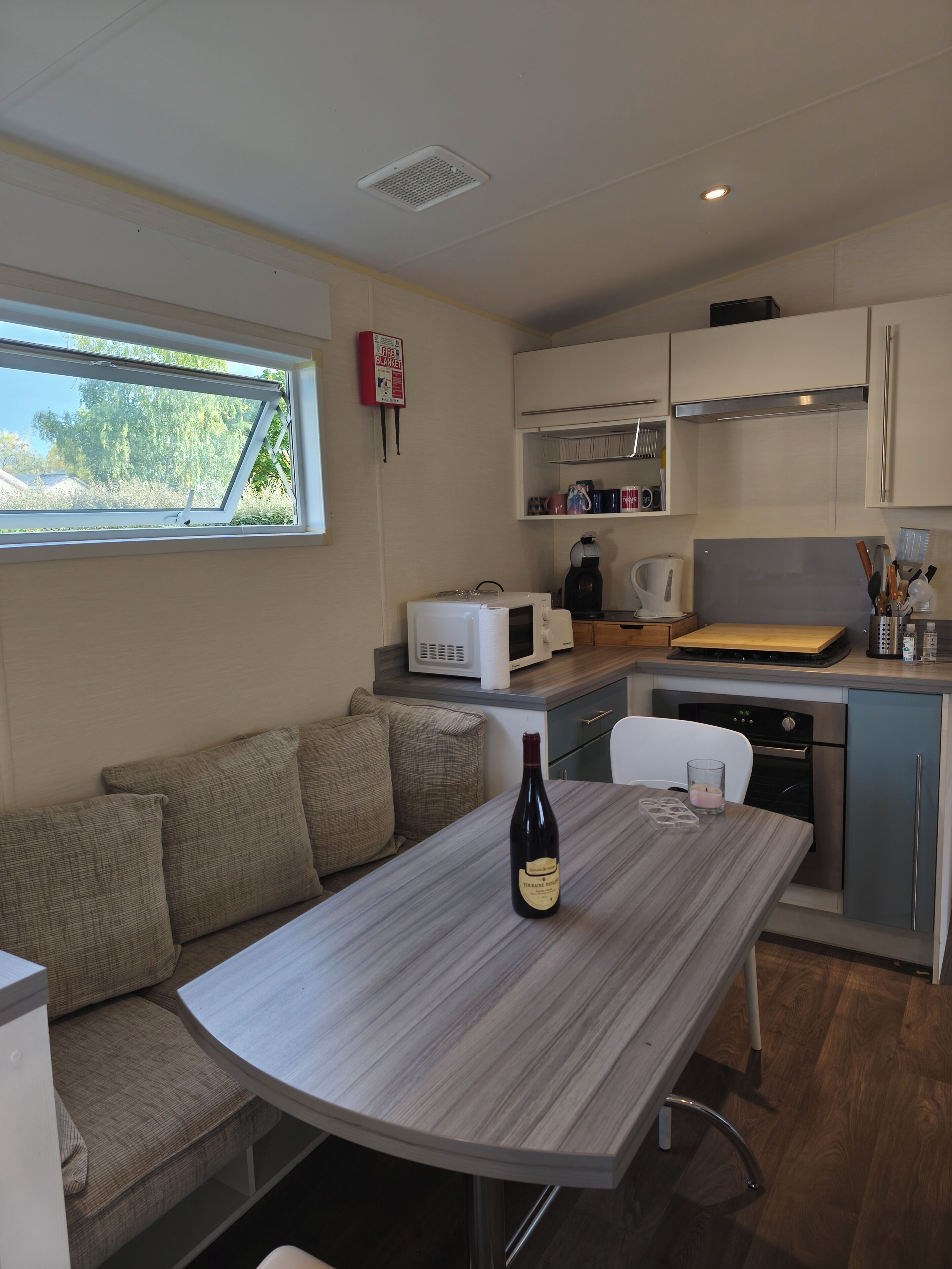 Una cocina compacta con área de comedor, microondas, cafetera y una botella de vino sobre la mesa.