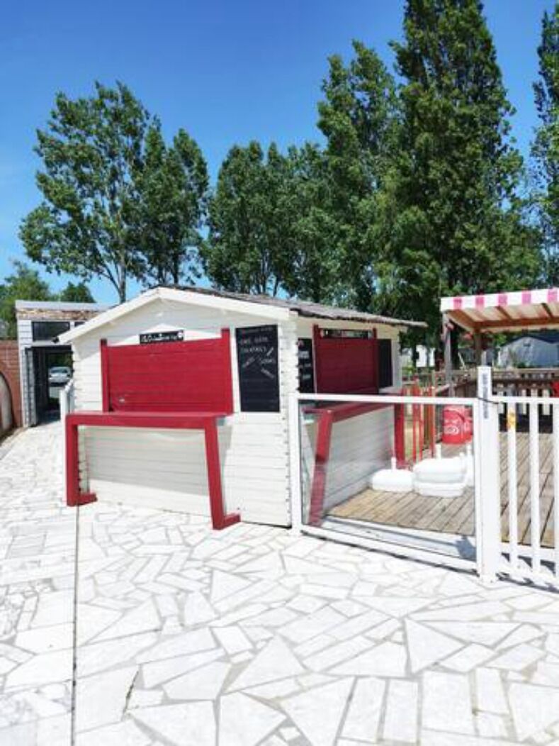 Un petit bâtiment blanc avec une porte rouge et un espace extérieur abrité doté d’une terrasse en bois.