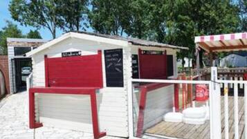 Un petit bâtiment blanc avec une porte rouge et un espace extérieur abrité doté d’une terrasse en bois.