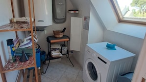 Ein kleiner Waschraum mit einer Waschmaschine, einem Wäscheständer, einem Tisch mit einem Korb und einem Fenster mit Blick.