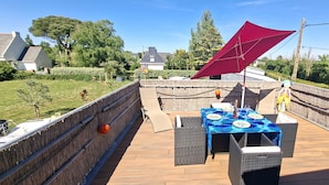 Eine Terrasse mit Esstisch, umgeben von Korbmöbeln und einer roten Markise.