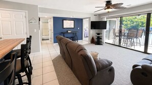 Ein modernes Wohnzimmer mit einer Couch, einem Esstisch und Stühlen, einem Fernseher und einem Balkon mit Gartenmöbeln.