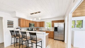 A modern kitchen with wooden cabinets, a stainless steel refrigerator, and a bar area with stools. - Lakeside Escape with Boat Slip (Rocky Mount)