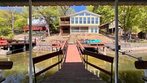 A wooden dock leading to a building with a balcony, surrounded by water and trees. - Lakeside Escape with Boat Slip (Rocky Mount)