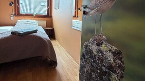 A bedroom with a bed, a window, and a wall-mounted artwork of a bird. - Guesthouse Leon (Torshavn)